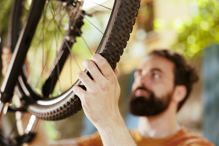 Detailaufnahme eines jungen Mannes, der den Fahrradreifen zum Zerlegen hält und greift, um ihn im Hof zu reparieren © freepik