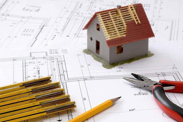 Symbolbild, welches ein Modellhaus mit Zange, Bleistift und Meterstab auf einem Bauplan zeigt © Pixabay