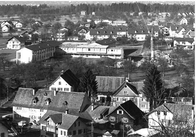 Blick vom Liebfrauenberg auf die am 25. September 1960 feierlich eröffnete Hauptschule Rankweil. Der Bau des Ostflügels wurde im Oktober 1965 gerade in Angriff genommen. Im Vordergrund der Gebäudekomplex Schleife 1 bis 5, im Hintergrund vor dem Auwald entlang der Frutz die noch weitgehend unbebaute Flur Bifang © Herbert Rauch